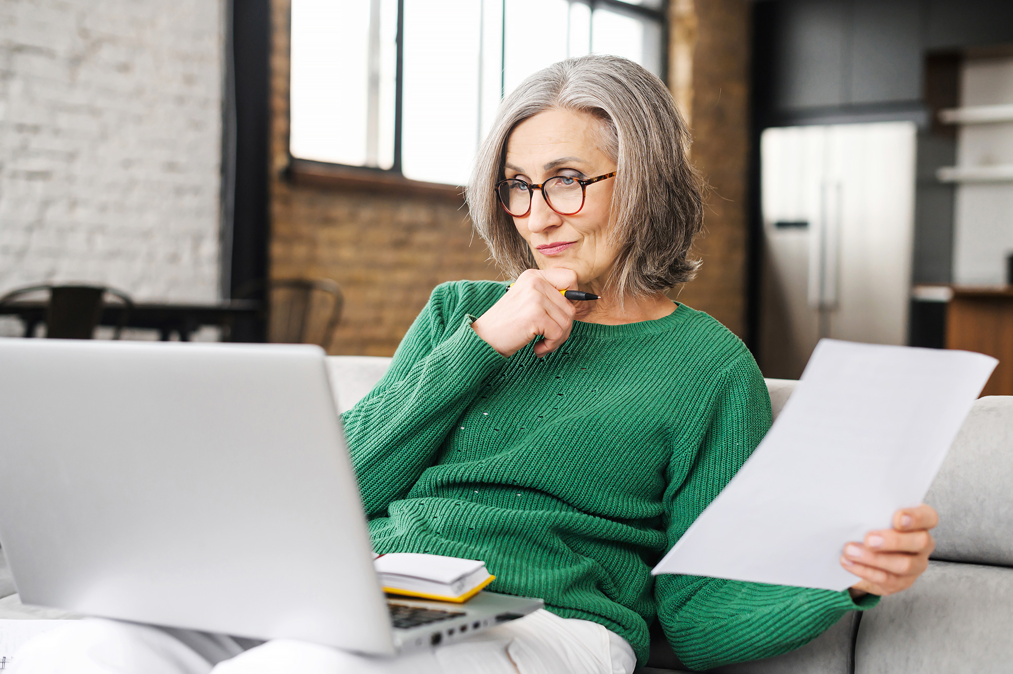 Woman wearing a green jumper looks inquisitively at a laptop